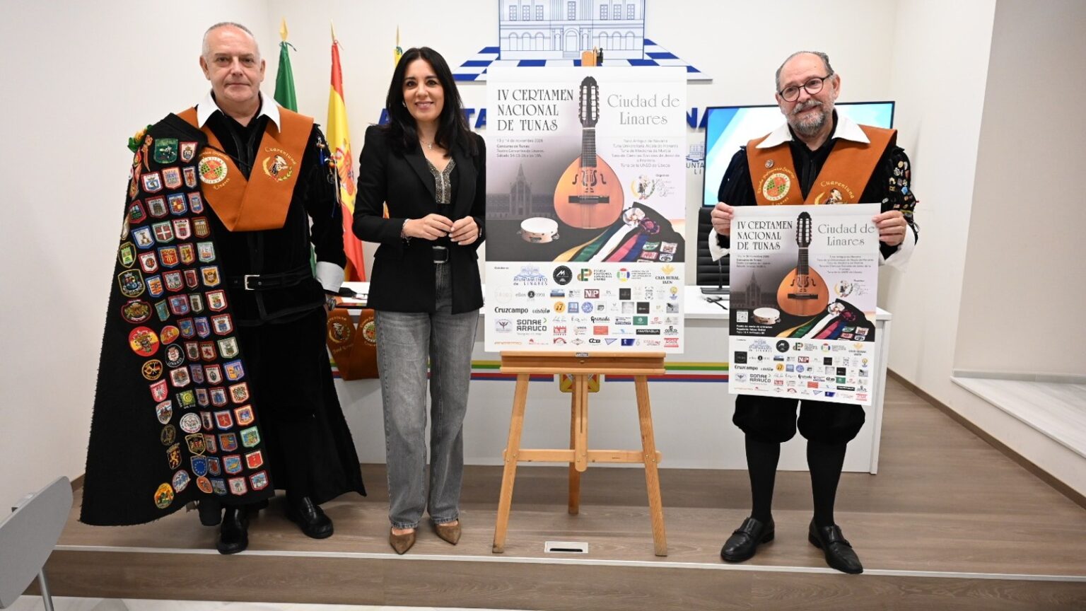 Dos tunos de la Cuarentuna Politécnica y la concejala de Cultura de Linares junto al cartel del IV Certamen Nacional de Tunas