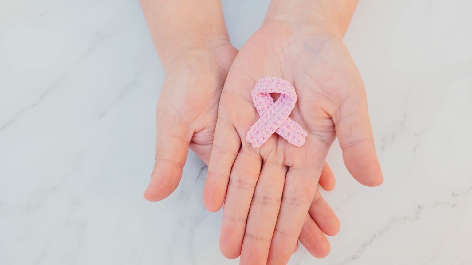 Lazo rosa, símbolo de la lucha contra el cáncer de mama, sostenido entre dos manos